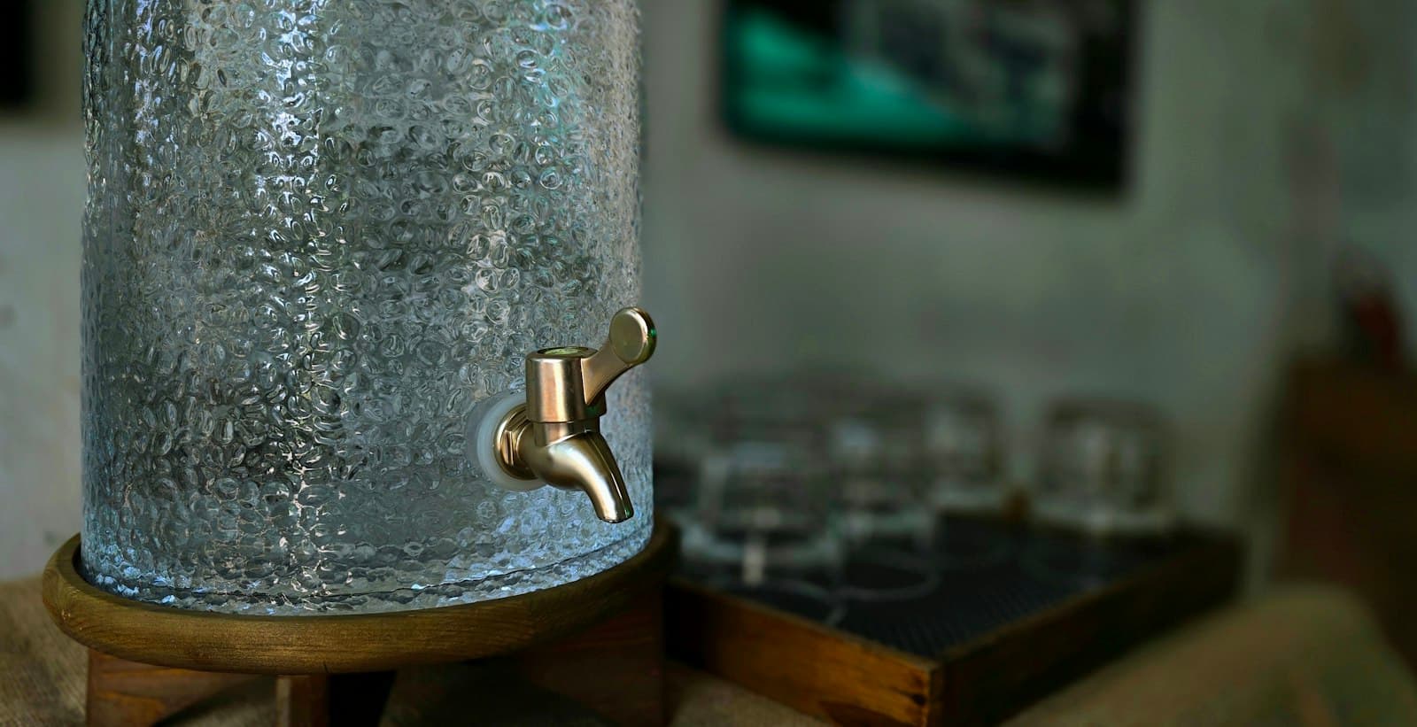 A glass water dispenser with a brass tap beside drinking glasses