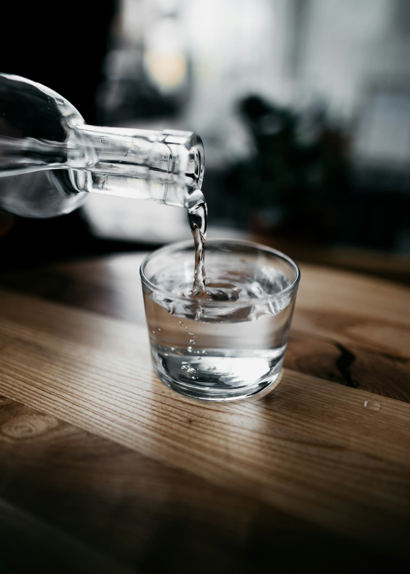 Water being poured from a bottle into a glass on a wooden table